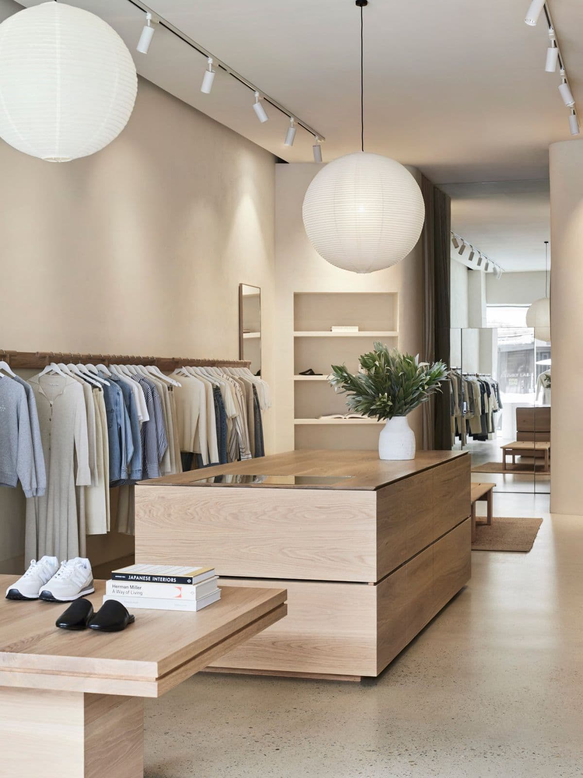 Minimalist clothing boutique with light wood furniture, neutral apparel, and large paper lantern lights.