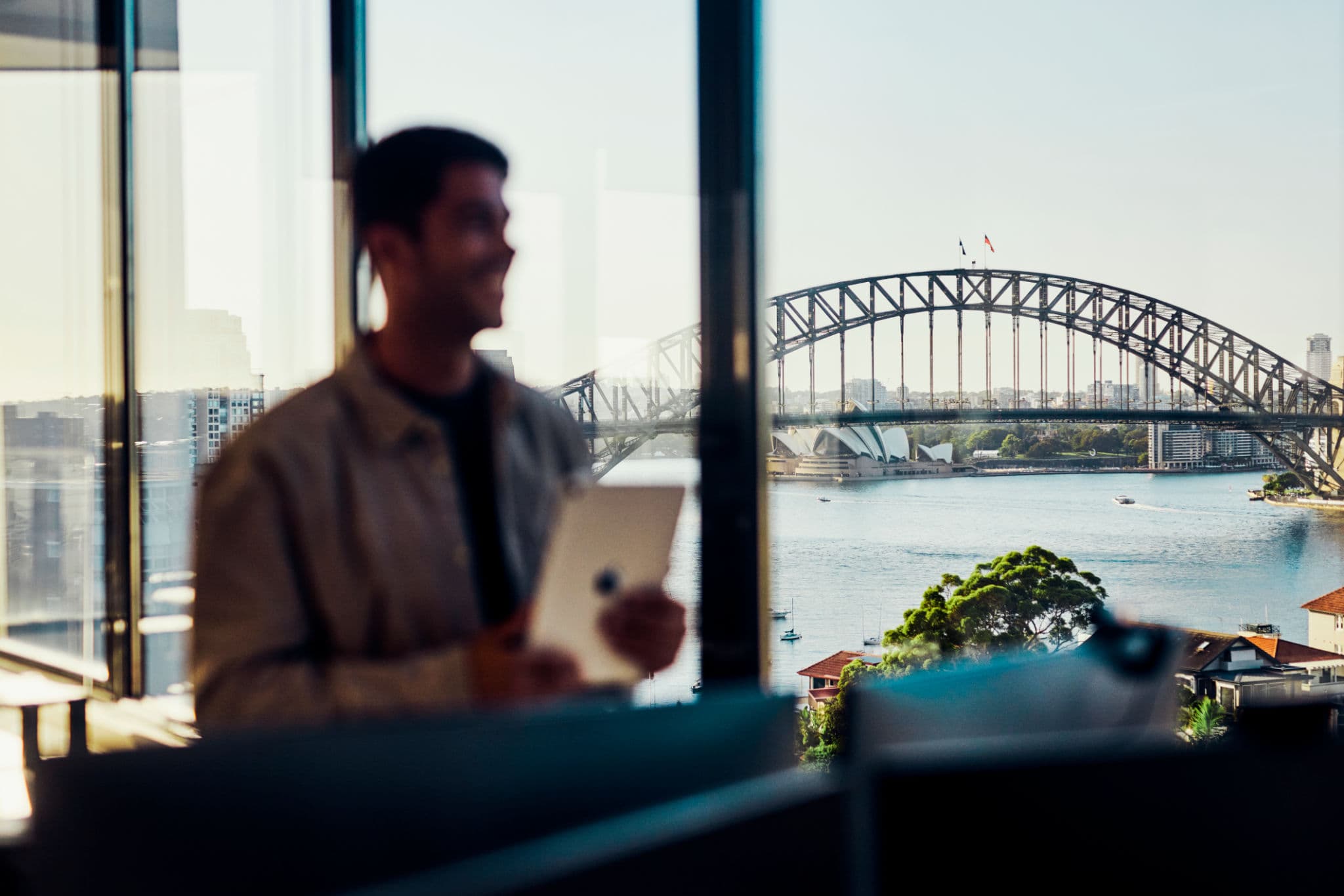 Blurred man with tablet looks out at the Sydney Harbour Bridge and Opera House.